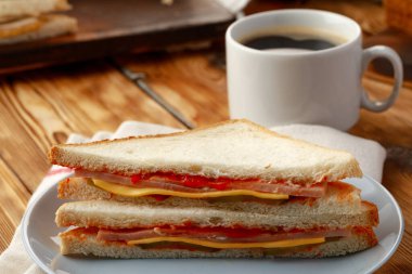 Tahta masadaki peçetede tost sandviçi ve bir fincan kahve.