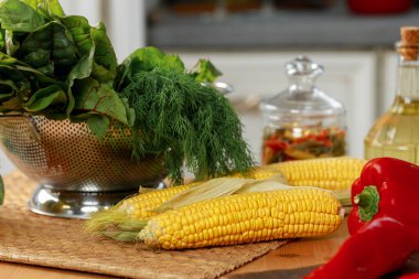 Tahta mutfak masasındaki mısır koçanları yakın.