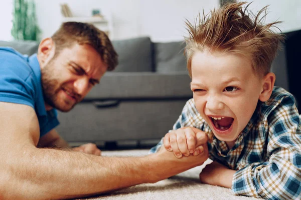 Father and son arm wrestling on carpet at home — Stock Photo, Image
