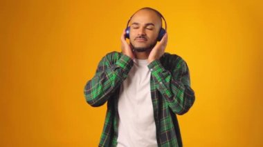 Yakışıklı Afro-Amerikalı adam sarı arka planda kulaklıkla müzik dinliyor.