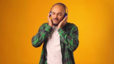 Yakışıklı Afro-Amerikalı adam sarı arka planda kulaklıkla müzik dinliyor.