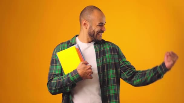 Estudiante afroamericano masculino sosteniendo libros y celebrando el éxito contra el fondo amarillo — Vídeos de Stock