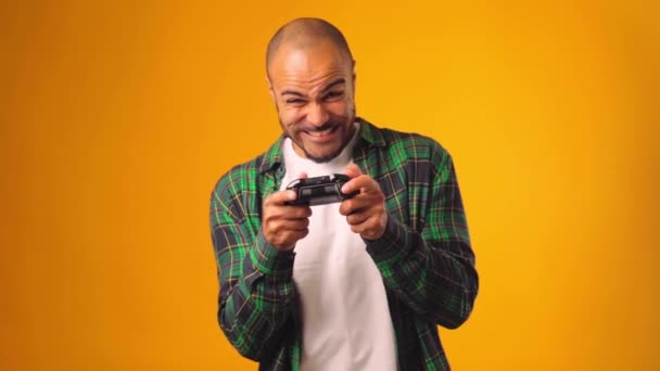 Fiatal afro-amerikai férfi játszik videojátékok joystick a kezében sárga háttér — Stock videók