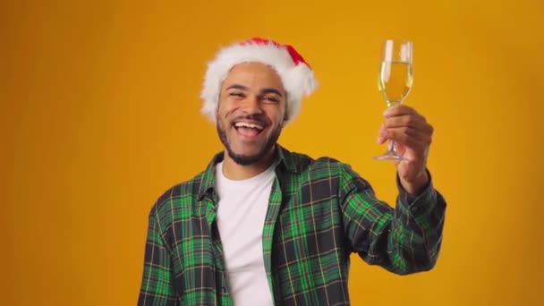 산타 모자를 쓴 아프리카계 미국인 남성, 노란색 배경에 대해 샴페인 한 잔을 들고 있는 모습 — 비디오