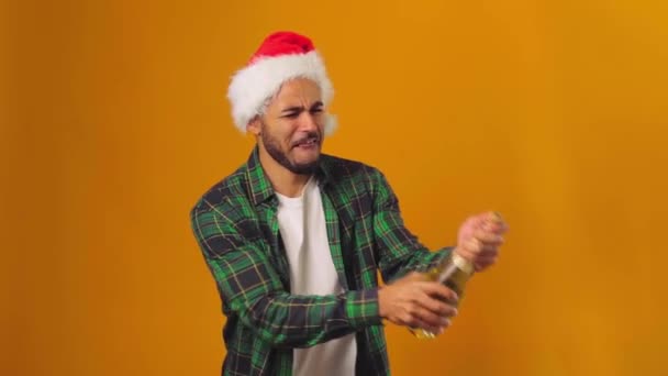 Hombre afroamericano en Santa sombrero apertura botella de champán con explosión sobre fondo amarillo — Vídeo de stock