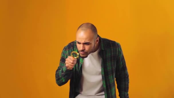 Young african american man looking through magnifying glass against yellow background — Stock Video