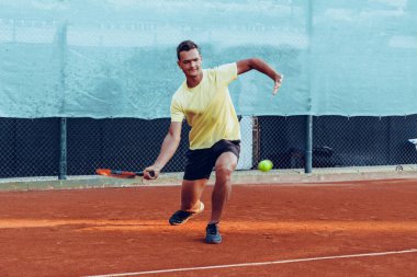 Genç yakışıklı adam tenis kortunda tenis oynuyor.