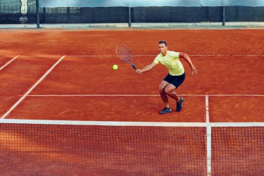 Genç yakışıklı adam tenis kortunda tenis oynuyor.