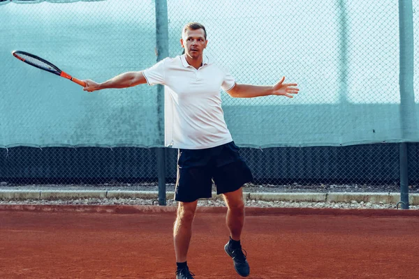 Молодой человек играет в теннис на открытом воздухе на теннисном корте утром — стоковое фото