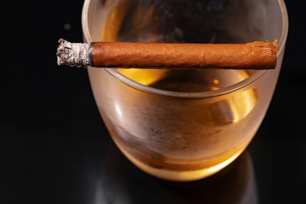 Cigare brûlant et verre de whisky sur fond noir — Photo