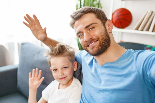 아버지 와아들은 소파에 앉아 카메라 앞에서 손을 흔들고 있다 — 스톡 사진