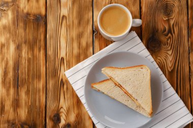 Tahta masadaki peçetede tost sandviçi ve bir fincan kahve.