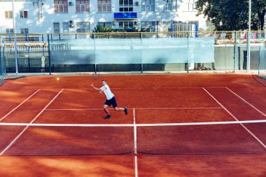 Adam uzaktan, kil tenis sahasında tenis oynuyor.