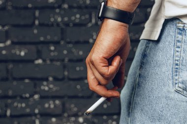 Siyah arka planda yanan sigarayı tutan erkek el.