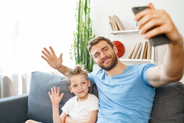 Padre e hijo haciendo una videollamada en el teléfono inteligente mientras están sentados en el sofá — Foto de Stock