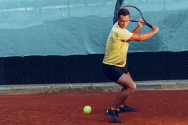 Genç yakışıklı adam tenis kortunda tenis oynuyor.