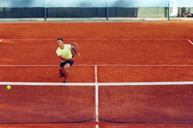Genç yakışıklı adam tenis kortunda tenis oynuyor.