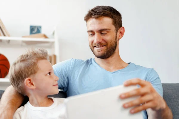 어린 소년과 그의 아버지는 함께 소파에 앉아 디지털 태블릿으로 비디오를 보고 있습니다 — 스톡 사진