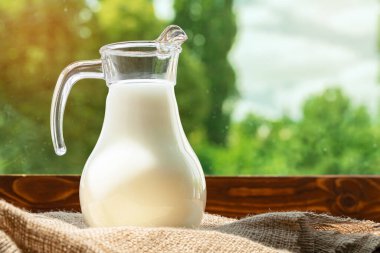 Tahta masanın üzerinde bulanık yeşilliklere karşı bir sürahi süt.