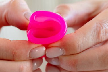 Beyaz kazaklı bir kadın elinde pembe bir fincanla ellerini kapatıyor.