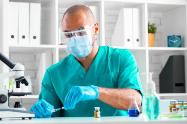 Afro-Amerikalı doktor masada oturuyor ve bir ilaç enjekte etmeye hazırlanıyor.