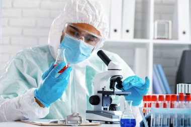 Mikroskop altında koruyucu elbise giyen bir tıp çalışanı.