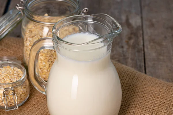 Glass pitcher of milk and oat flakes on wooden table