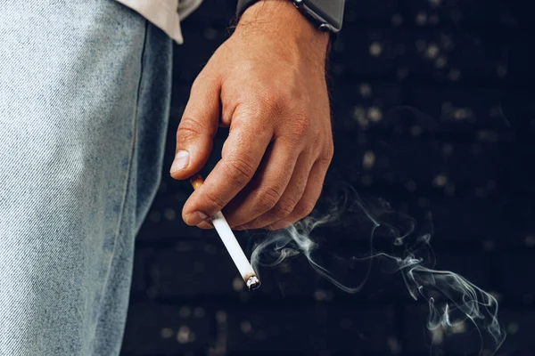 Muž ruka drží zapálenou cigaretu na černém pozadí — Stock fotografie