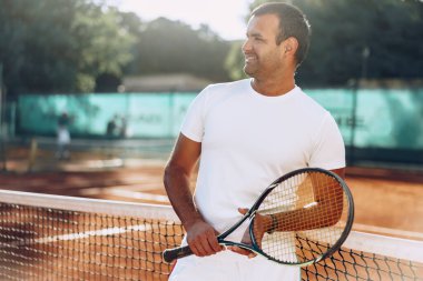 Tenis raketli Spoty adam kil kortunun yanında duruyor.