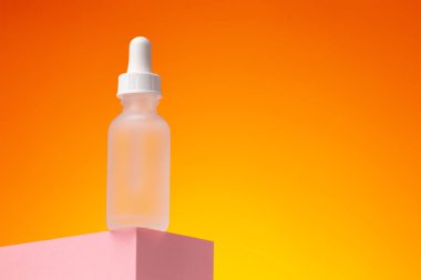 Turuncu arka planda pipetli güzellik yağı şişesi.