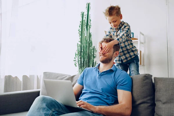 Kleiner Junge bedeckt Vater mit den Händen im Wohnzimmer — Stockfoto