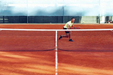 Genç yakışıklı adam tenis kortunda tenis oynuyor.