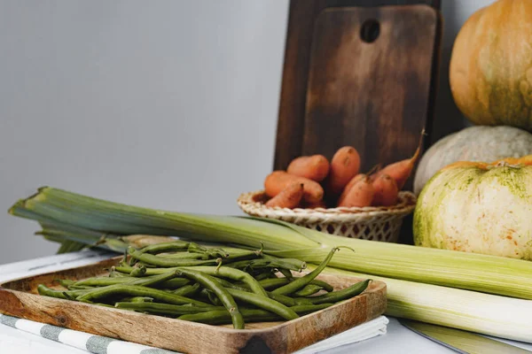 Haricots verts dans une assiette et autres légumes sur la table de cuisine — Photo