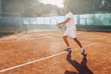 Formda adam tenis sahasında tenis oynuyor.