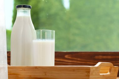 Şişe ve bir bardak süt ahşap masada bulanık yaprak arka planına karşı.