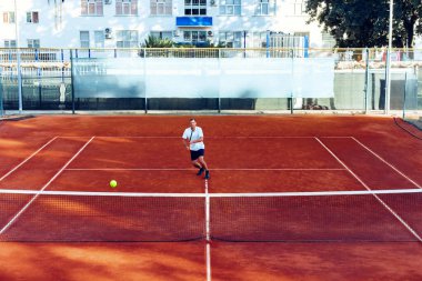 Adam uzaktan, kil tenis sahasında tenis oynuyor.