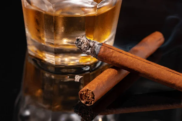 Vaso de whisky y cigarro encendido sobre fondo negro — Foto de Stock