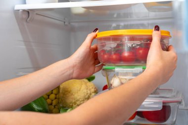 Kadın eli buzdolabından yiyecek dolu bir kutu alıyor.