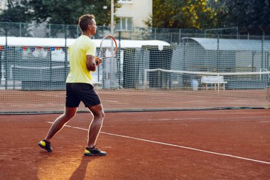 Genç yakışıklı adam tenis kortunda tenis oynuyor.