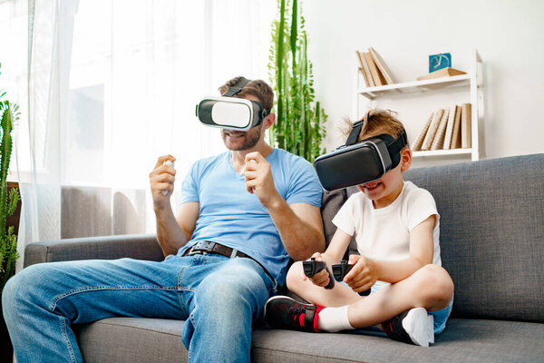 Dad and son sitting on sofa and playing games with VR glasses