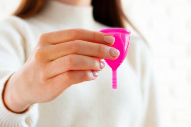 Beyaz kazaklı bir kadın elinde pembe bir fincanla ellerini kapatıyor.