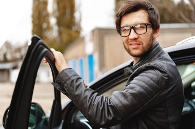 Gözlüklü şık bir adam arabada oturuyor.