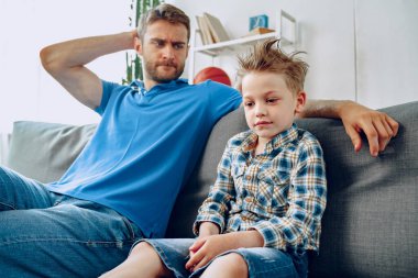 Baba, evdeki kanepede otururken küçük oğluyla konuşuyor.