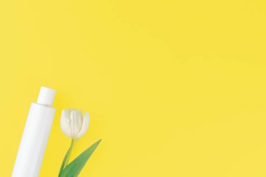 Aydınlatıcı sarı arkaplan üzerinde lale bulunan beyaz kozmetik kabın üst görünümü