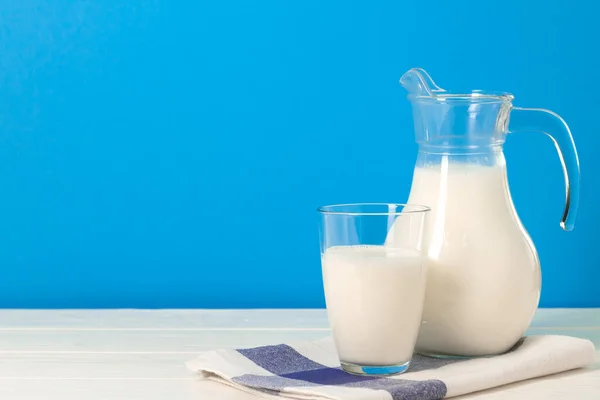 Mavi arka plana karşı bardak ve sürahi süt — Stok fotoğraf