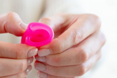 Beyaz kazaklı bir kadın elinde pembe bir fincanla ellerini kapatıyor.