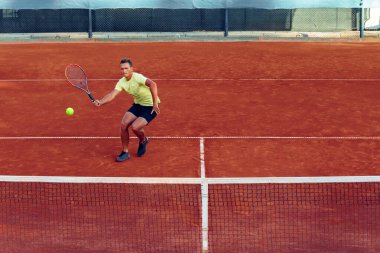 Genç yakışıklı adam tenis kortunda tenis oynuyor.
