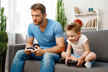 Babası ve küçük oğlu evde video oyunu oynuyorlar.