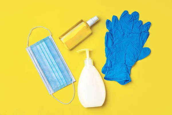 Mascarilla facial, guantes, jabón y desinfectante sobre fondo amarillo iluminante — Foto de Stock
