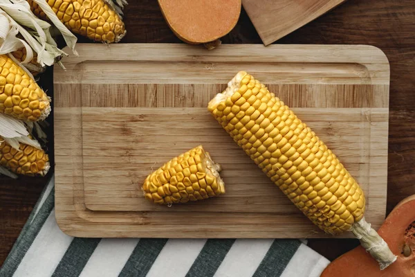 Corn cob and pumpkin on brown wooden board — Stock Photo, Image